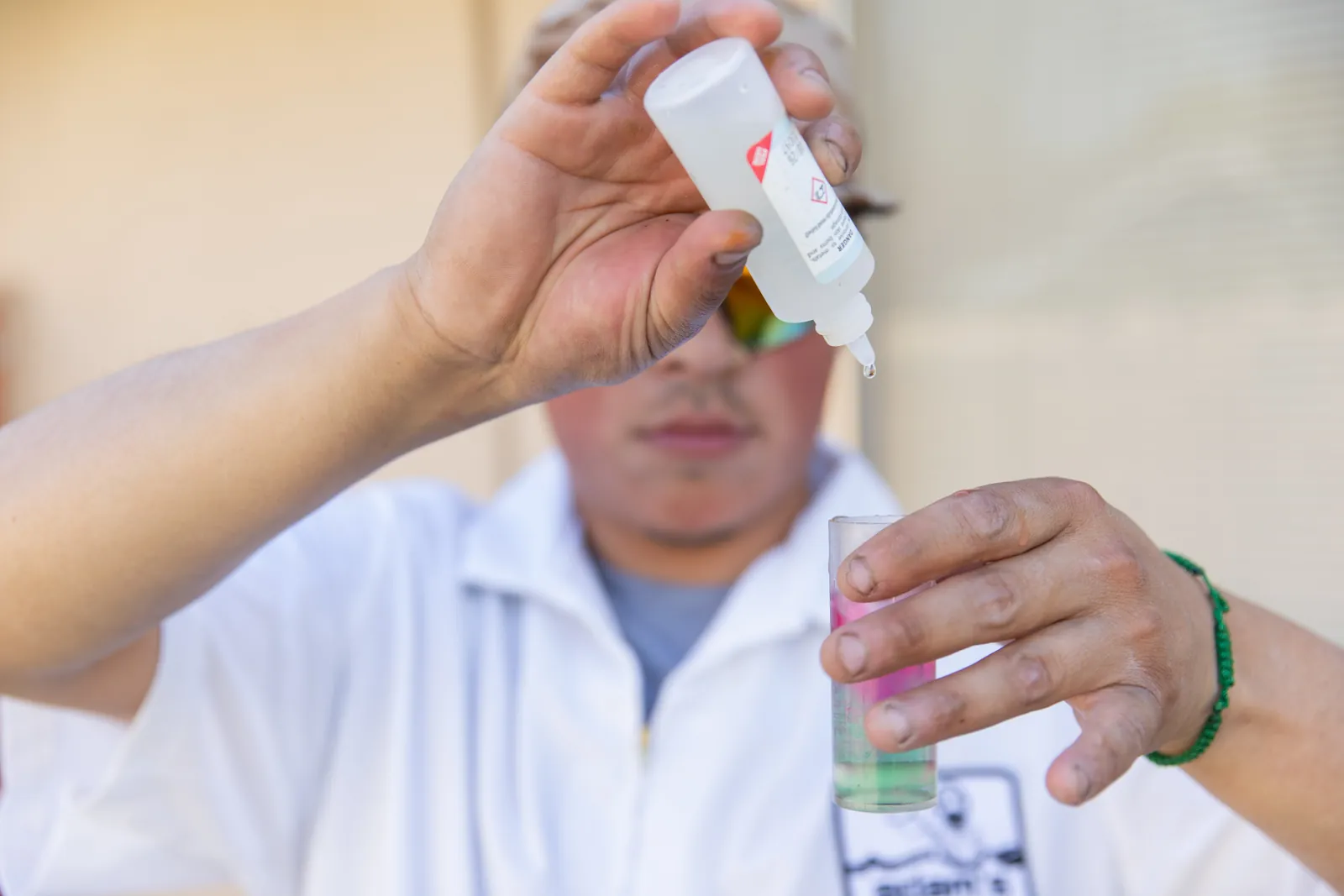 Person wearing white lab coat examines a small white object held in their hand.