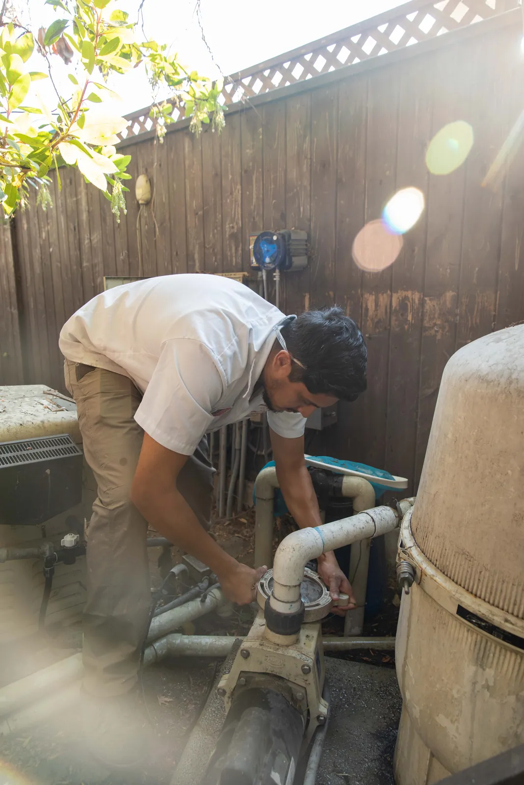Person in white shirt and cap working on cylindrical pool system components outdoors.