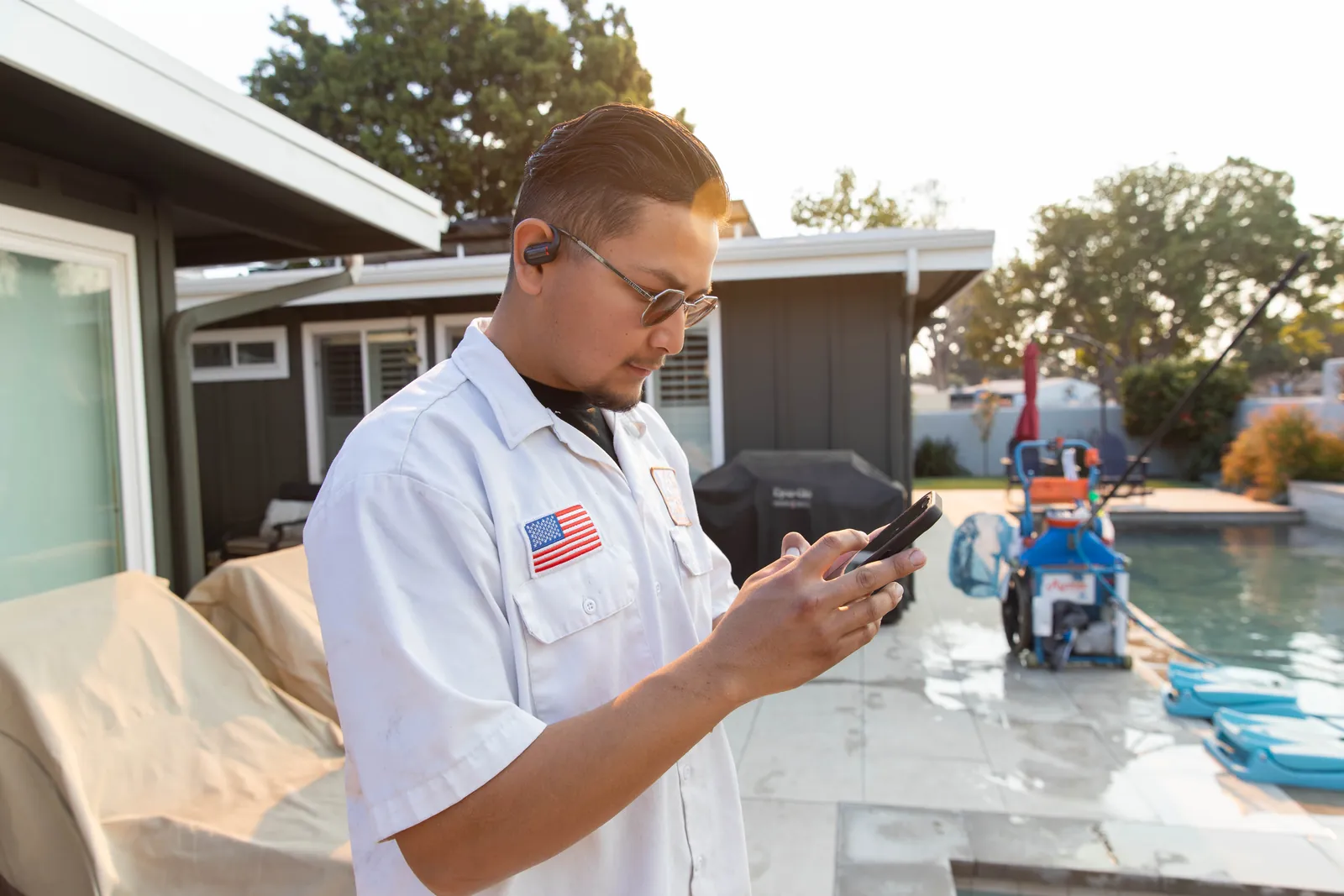 Man in light blue shirt holding water sample vial, pool and equipment visible in background.