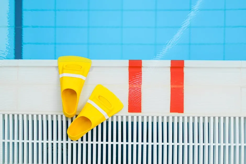 Pair of yellow swim fins resting on the white edge of a lap pool
